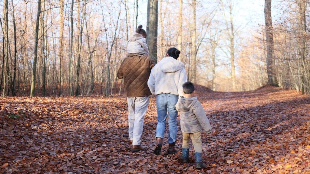 Family enjoys a walk through a forest in autumn, surrounded by fallen leaves.